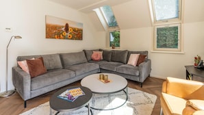 Un salon moderne avec un canapé d’angle gris, une table basse ronde et un tableau représentant un champ de tournesols.