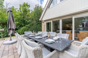 An outdoor dining area with a long table, wicker chairs, and a large umbrella. - Charming Country House for 6 People (De Koog)