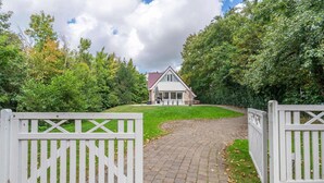 Une maison avec une allée pavée menant à une entrée fermée par un portail, le tout entouré d’une végétation luxuriante.