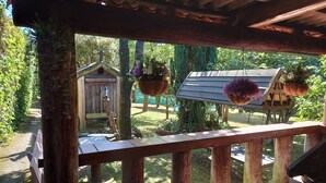 Una terraza de madera con barandilla, un comedero para pájaros y cestas colgantes de flores.
