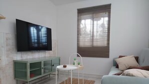 Una sala de estar con un televisor montado en la pared, un mueble verde, una mesa redonda blanca con una planta, un tapete marrón y un sofá azul claro.