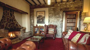 A cozy living room with a stone fireplace, leather furniture, a chess table, and a bookshelf. - Noddfa Country House (Harlech)