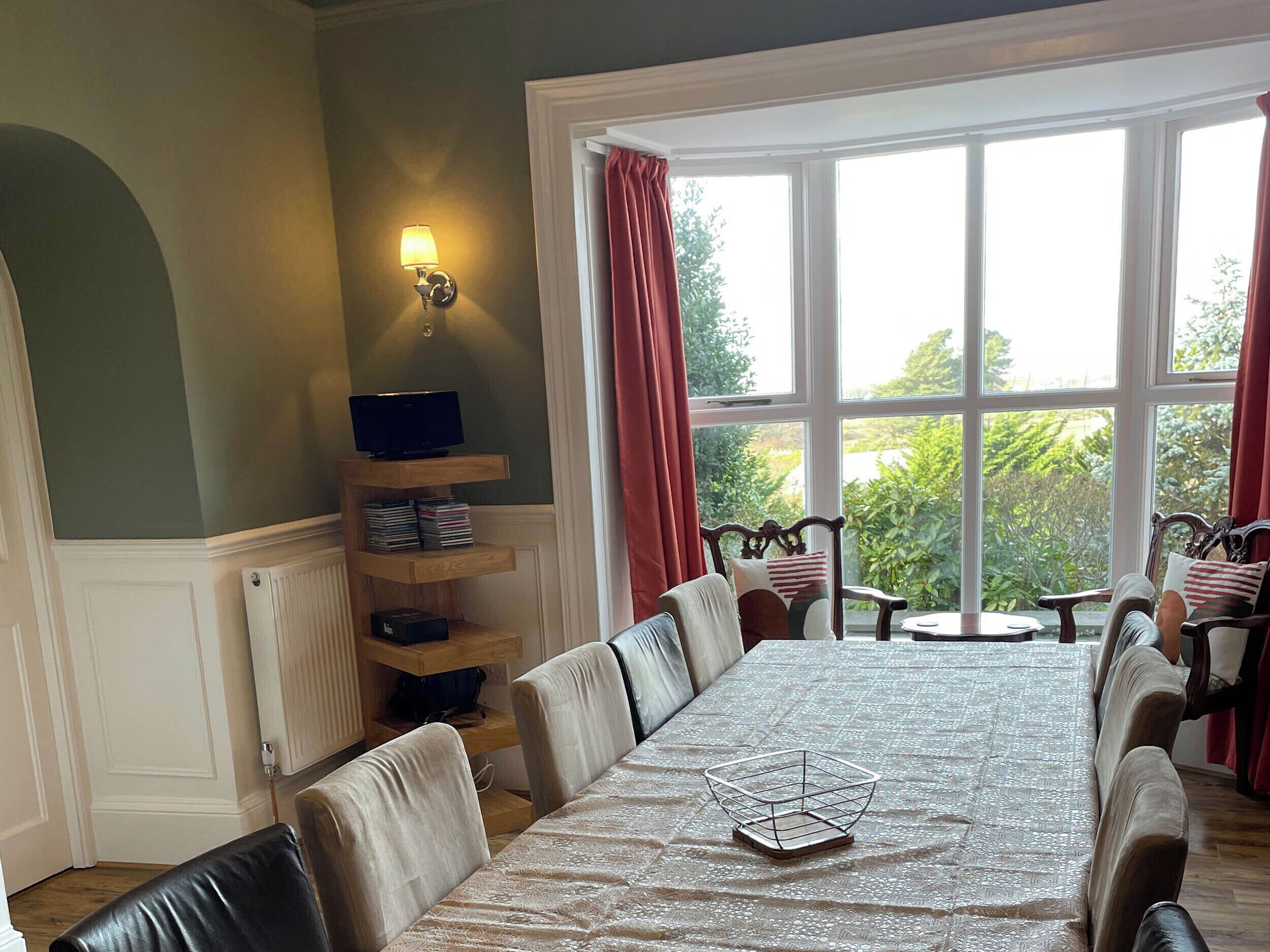 A dining area with a long table, chairs, a buffet shelf, and a window with curtains.