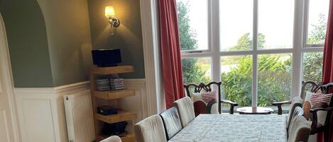 A dining area with a long table, chairs, a buffet shelf, and a window with curtains.