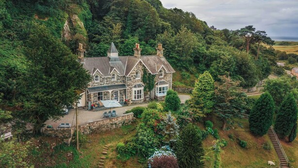 A large stone house with a prominent tower, surrounded by lush greenery and a well-maintained garden. - Noddfa Country House (Harlech)