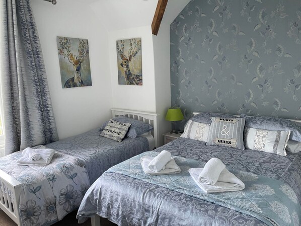 A bedroom with two beds, each with floral-patterned bedding and pillows, a nightstand with a lamp, and two wall-mounted paintings.