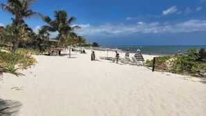 Ein Strand mit weißem Sand, Palmen und Strandsonnenschirmen.