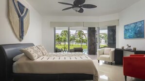 A modern bedroom with a bed, a ceiling fan, a large window with a view of palm trees, and a red chair.
