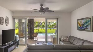 A modern living room with a large grey sofa, a flat-screen TV, and a ceiling fan.
