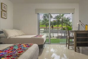 Ein Schlafzimmer mit Bett, Schreibtisch und Blick auf einen Garten durch eine Schiebetür.
