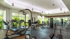 A spacious gym with various exercise equipment, large windows, and a high ceiling.