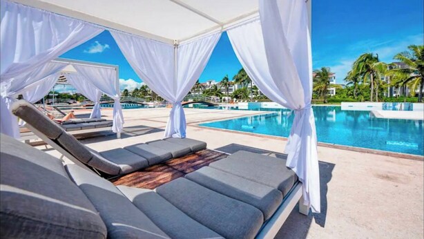 A poolside lounge area with white canopies, lounge chairs, and a clear view of the pool and surrounding palm trees.