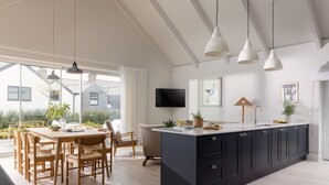 Una cocina moderna con una isla grande, una mesa de comedor de madera y sillas. Hay un televisor montado en la pared y un ventanal que ofrece vistas al exterior.