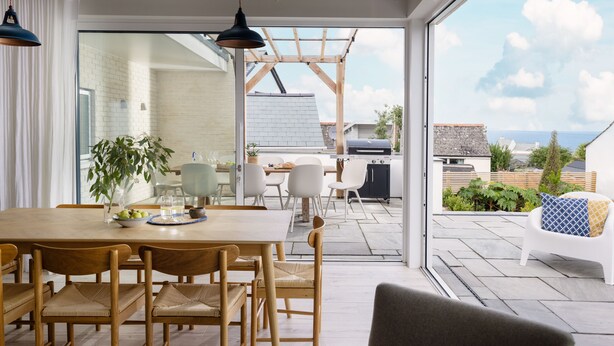 Un comedor moderno con una mesa y sillas de madera, una planta en maceta, y vistas al patio exterior y la zona de la cocina.