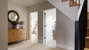 Un interior moderno con una escalera de madera, un espejo redondo, un mueble de madera y una puerta que da a otra habitación.