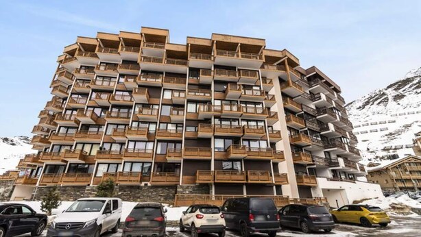 A multi-story building with balconies, a parking lot with several cars, and a mountainous backdrop. - VAL Thorens Rental: Spacious 2-room Apartment for 6 With 3 Sunny Balconies (Les Belleville)