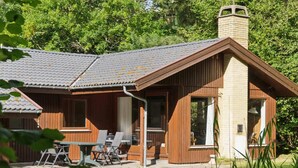En træhytte med skorsten, store vinduer og en terrasse med udendørs møbler.