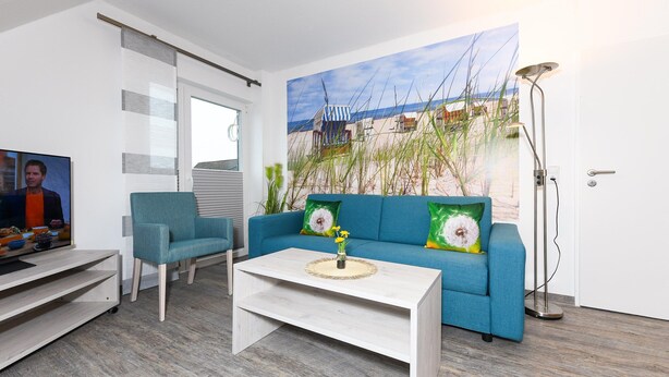 A living room with a blue sofa, a white coffee table, and a painting of a beach scene. - Gemuetliche Ferienwohnung im Obergeschoss, Bensersiel (Esens)