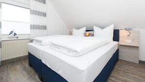 A neatly made bed with white linens, a small sailboat by the window, and a bedside table with a lamp. - Gemuetliche Ferienwohnung im Obergeschoss, Bensersiel (Esens)