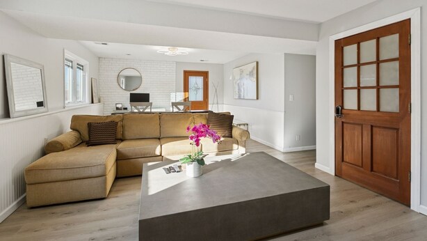 A modern living room with a beige sectional sofa, a coffee table with a vase of flowers, and a wooden door with glass panels.