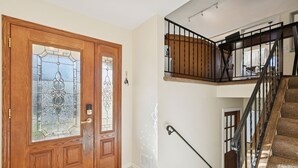 A wooden front door with glass panels, a staircase with a black railing, and a white tiled floor.