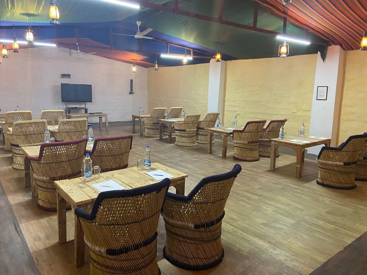 A restaurant with wicker furniture, tables, and hanging lights.