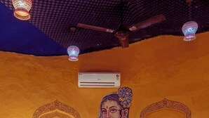 Et værelse med seng, ventilator, aircondition og vægmonteret lysarmatur.