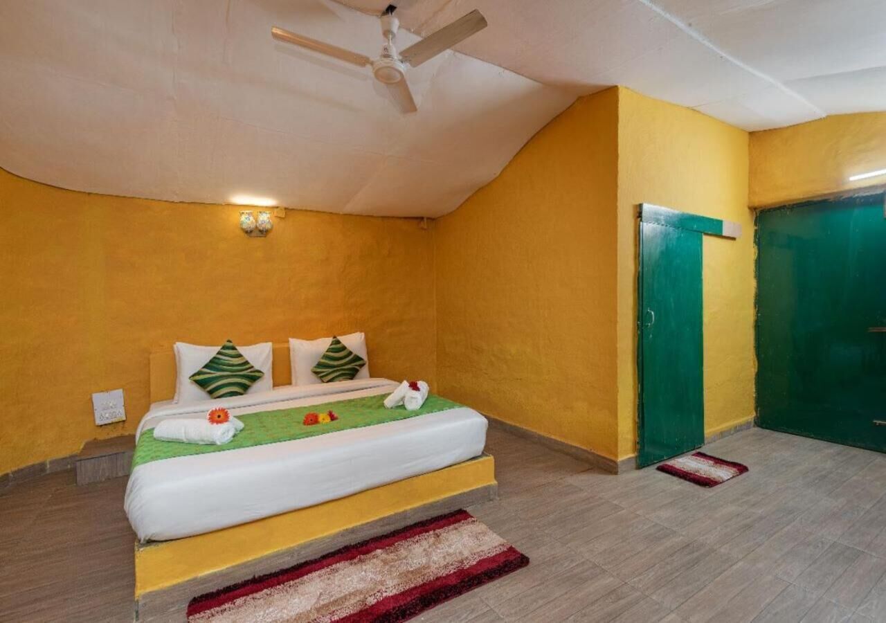 A single bed with a white mattress, green and white pillows, and a red and white striped rug.