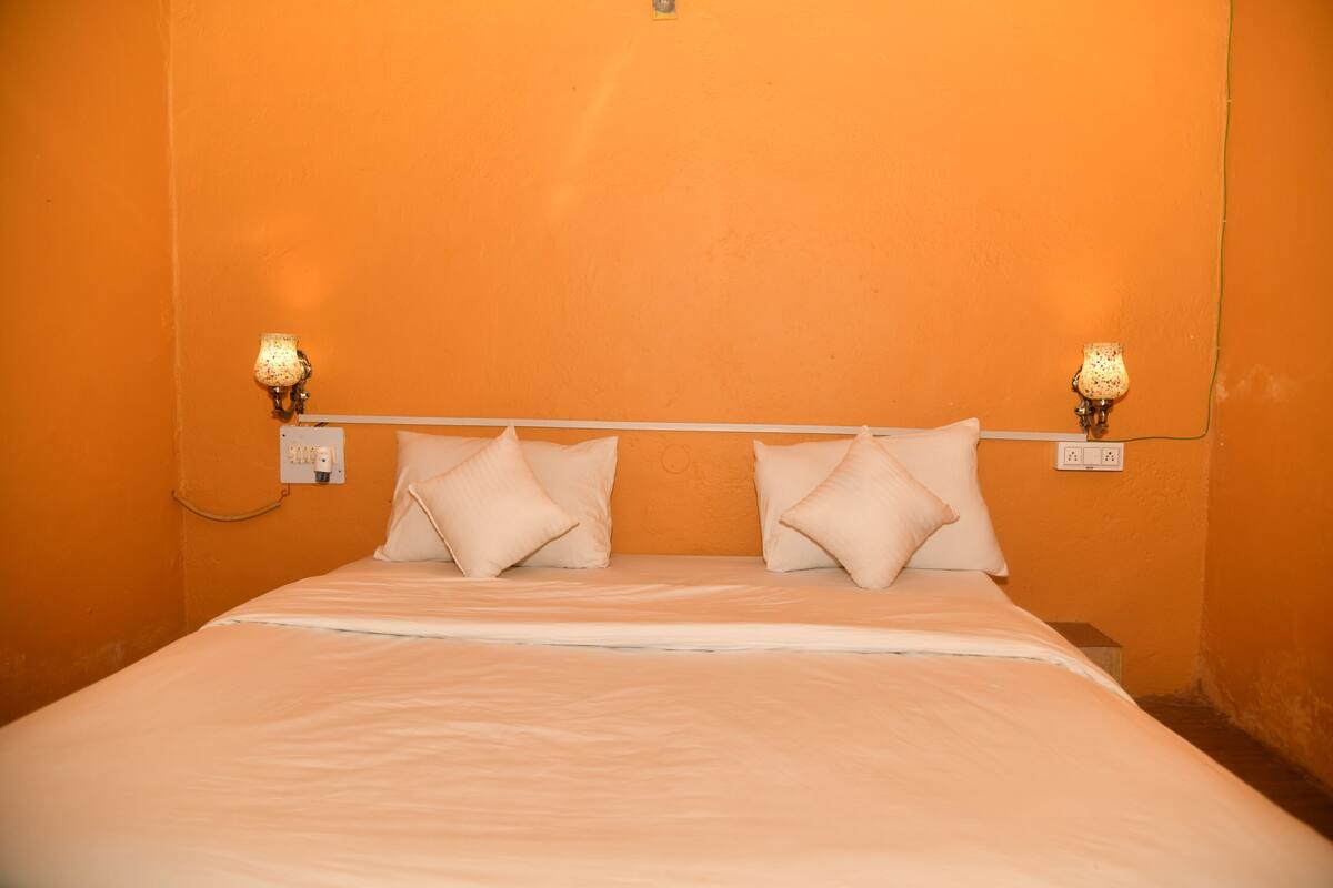 A bed with white linens, two bedside lamps, and a plain orange wall.