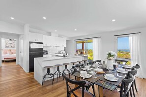 Una cocina moderna con armarios blancos, un refrigerador negro y un comedor con una isla grande, taburetes de bar y una mesa preparada para cuatro.