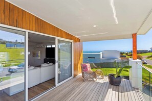 Un balcon moderne avec une terrasse en bois, une porte vitrée donnant sur l’espace de vie et une vue sur la mer.