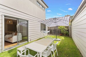Eine Terrasse mit Tisch und Stühlen, einem gestreiften Sonnenschirm und einer Glastür, die in einen Wohnbereich führt.