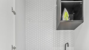Pequeña área de lavandería con lavadora de carga frontal, un lavabo y un estante con un objeto verde.