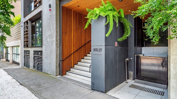 Entrada moderna de un edificio con techo de listones de madera, una escalera y un letrero que dice "HOLLY".