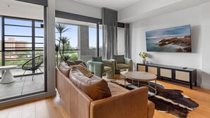 Una sala moderna con un sofá de cuero, dos sillones, una mesa redonda de centro y un televisor plano grande sobre un mueble negro.