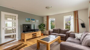 A modern living room with a sofa, a coffee table, a TV, and a wooden cabinet. - Villa With Finnish Sauna and Outdoor Shower (De Koog)