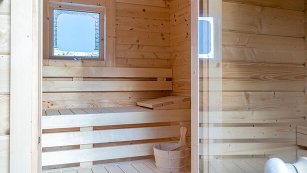 A wooden sauna with a window, wooden benches, and a bucket. - Villa With Finnish Sauna and Outdoor Shower (De Koog)