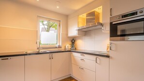 A modern kitchen with white cabinets, a stainless steel oven, and a window providing natural light. - Villa With Finnish Sauna and Outdoor Shower (De Koog)