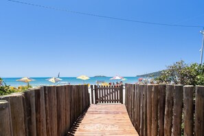 A wooden pathway leading to a beach with umbrellas and people in the background.