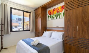 Una habitación de hotel con cama, una ventana con cortinas, un armario de madera y un cuadro de tulipanes.