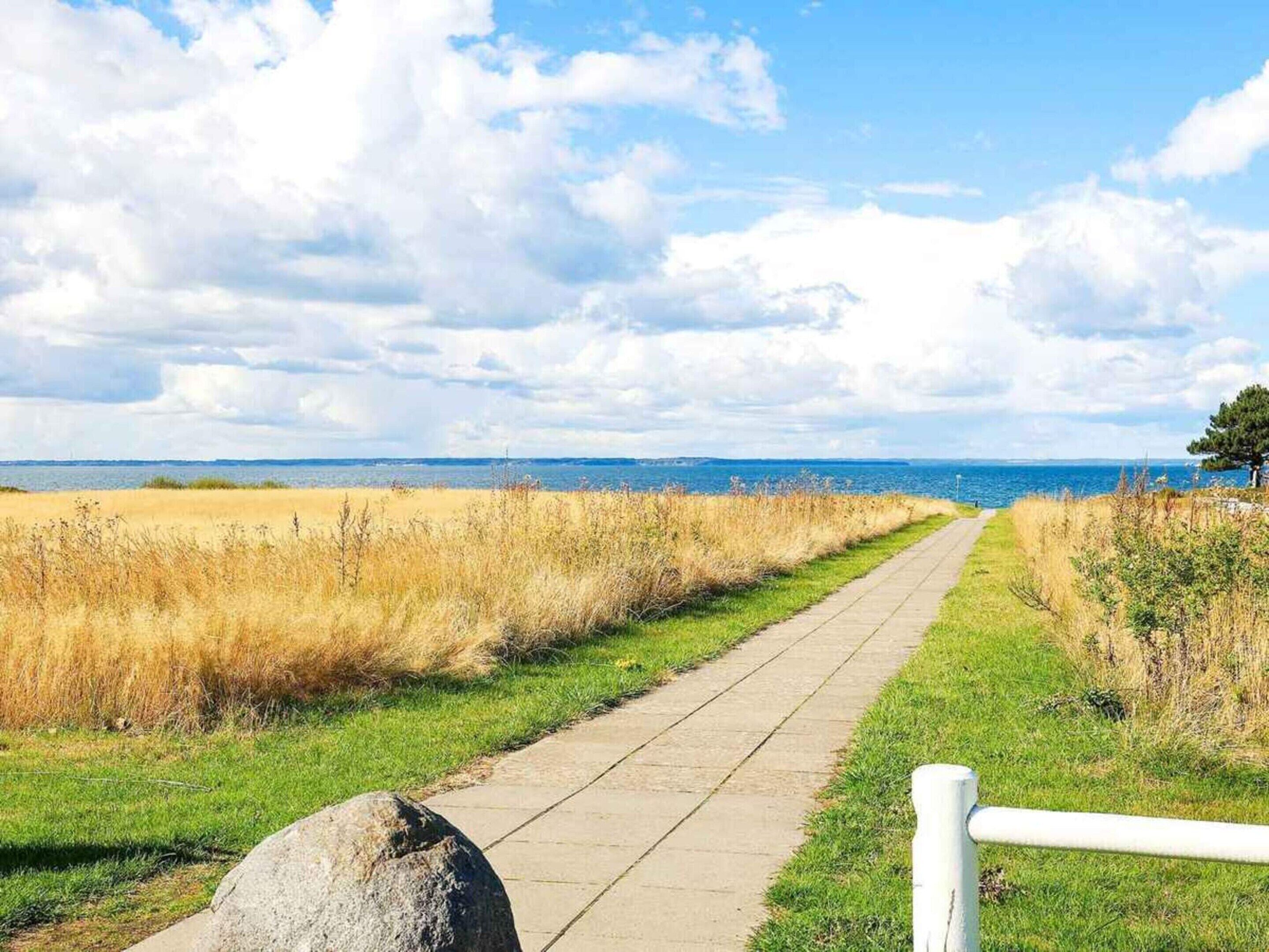 Un sentier pavé mène à un plan d’eau, entouré de prairies verdoyantes et surplombé d’un ciel dégagé.