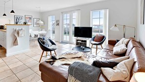 Ein modernes Wohnzimmer mit einer Ledersofa, einem Flachbildfernseher und einem Essbereich mit weißem Tisch und Stühlen.