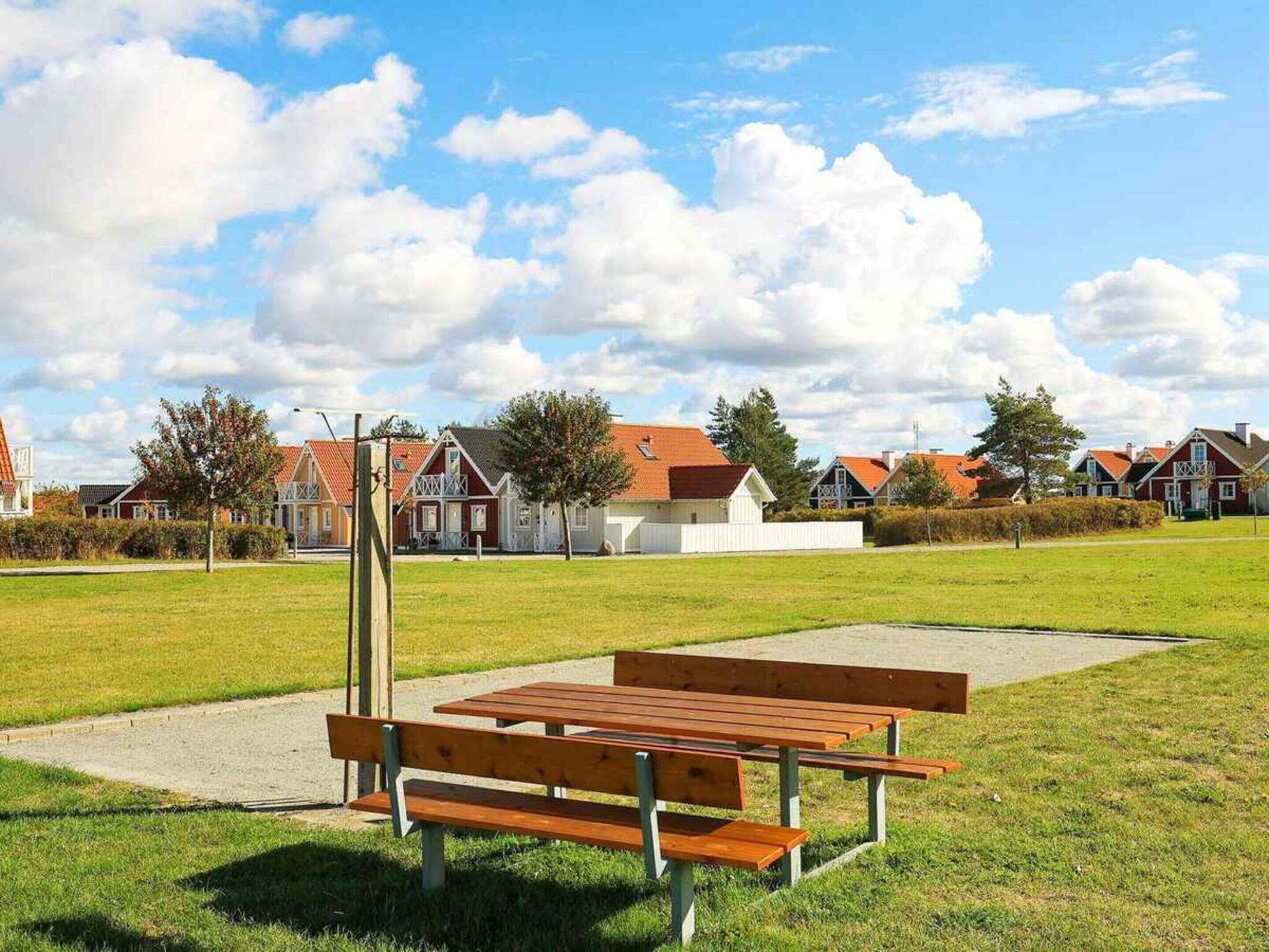 A park with a wooden bench and picnic table, surrounded by houses with red roofs.