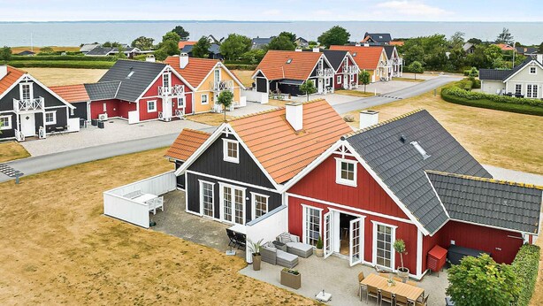 Eine Reihe roter und weißer Häuser mit grauen Dächern, einer gepflasterten Auffahrt und Blick auf das Meer.
