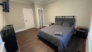 A bedroom with a large bed, a TV mounted on the wall, a door, and a small table. - 2BR Apartment Near Wesleyan 102 (Middletown)