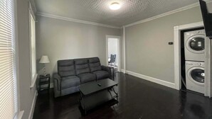 A living room with a dark-colored sofa, a small table, and a washing machine. - 2BR Apartment Near Wesleyan 102 (Middletown)