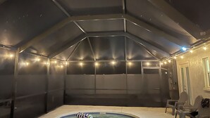 Un pati tancat amb un banyera d'hidromassatge, llums lluminoses i dues cadires.