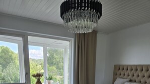 Ett sovrum med en stor säng, en kristallkrona, utsikt över grönskan utanför och en krukväxt på fönsterbrädan.