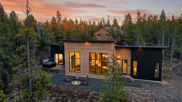 A modern cabin with large windows, a deck, and a fire pit.