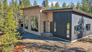 A modern two-story cabin with large windows, a wooden deck, and a surrounding forest.